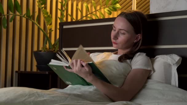 Beautiful woman reading favourite book at night before going to sleep. — Stock Video