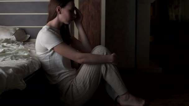 슬픈 여자가 침대 옆 바닥에 앉아 있다. 좌절 한 여자가 혼자 앉아서 무릎을 안고 시선을 돌리는 모습. — 비디오