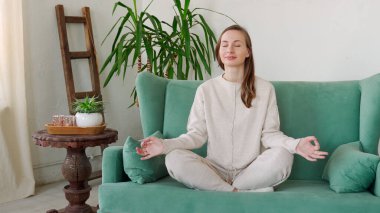 Genç bir kadın oturma odasında kanepede oturur yoga çalışır evde negatif duyguları hafifletir.