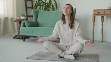 Nilüfer pozisyonunda yoga ve meditasyon yapan bir kadın evinde yerde oturuyor.