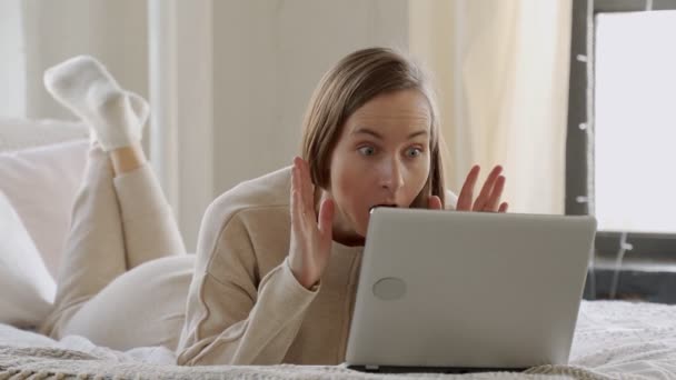 Überraschte junge Frau schaut auf ihren Laptop und schaut sich im Bett liegende Inhalte an — Stockvideo