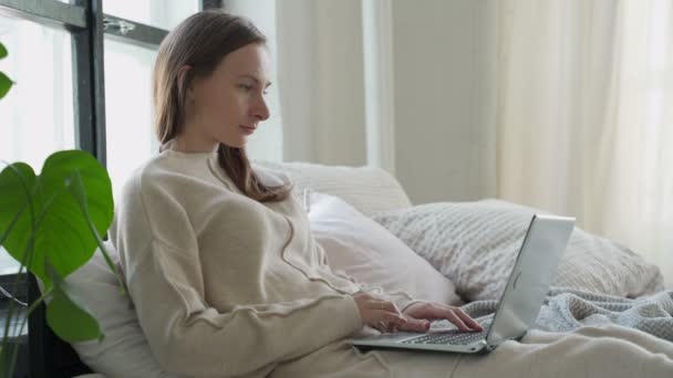 Zrelaksowany brunetka młoda kobieta za pomocą laptopa w łóżku w domu — Wideo stockowe