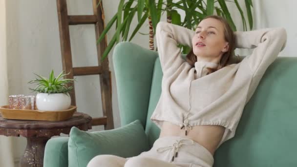 Stanco giovane donna sta riposando in una comoda sedia con le mani dietro la testa — Video Stock