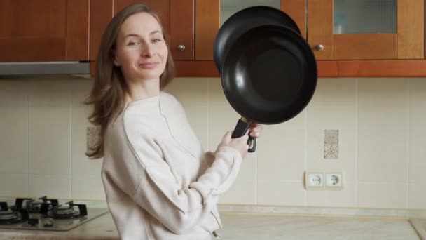 Souriant femme attrayante garde deux nouvelles poêles à frire dans sa cuisine — Video