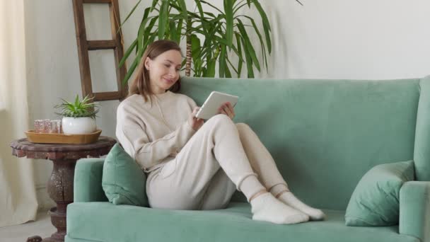 Beautiful young brunette woman using tablet sitting on sofa at home at living room — Stock Video