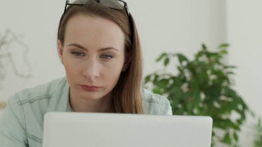 Güzel genç bir kadın dikkatle bir dizüstü bilgisayarla çalışıyor. Kadınların yüzü yakındır.