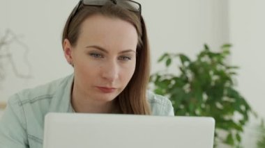 Güzel genç bir kadın dikkatle bir dizüstü bilgisayarla çalışıyor. Kadınların yüzü yakındır.