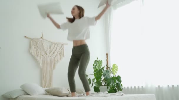 Νεαρή αστεία γυναίκα πηδάει στο κρεβάτι με ένα μαξιλάρι στην κρεβατοκάμαρα — Αρχείο Βίντεο