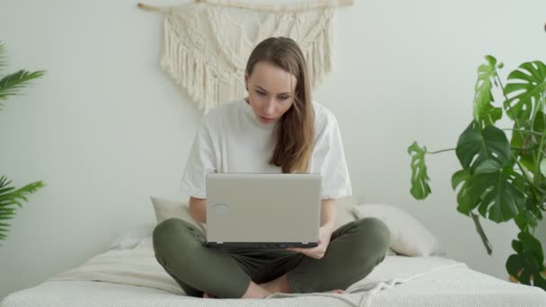 Junge Frau sitzt mit Laptop auf dem Bett und feiert Sieg oder Erfolg — Stockvideo