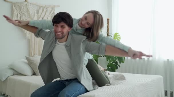 Mulher feliz piggyback seu namorado no quarto, homem forte carregando amante em suas costas, cônjuges jogando jogo engraçado — Vídeo de Stock