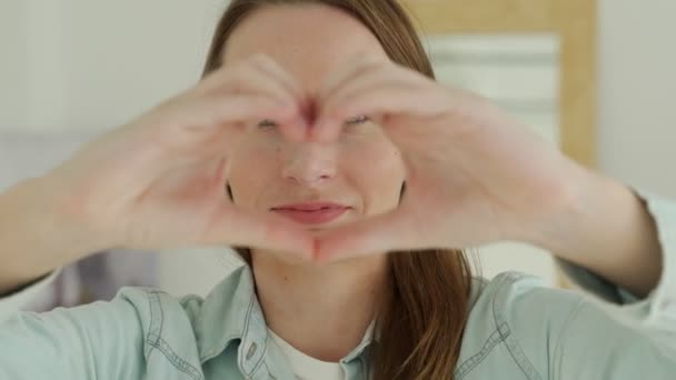Mujer joven sonríe y hace una forma de corazón con sus dedos — Vídeos de Stock