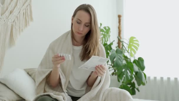 Una donna legge le istruzioni mediche prima di prendere le pillole sedute sul letto nella sua camera da letto — Video Stock