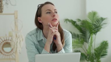 Dizüstü bilgisayarla çalışan genç bir kadın çenesini açıp düşünüyor, düşünceli bir ifade takınıyor.. 