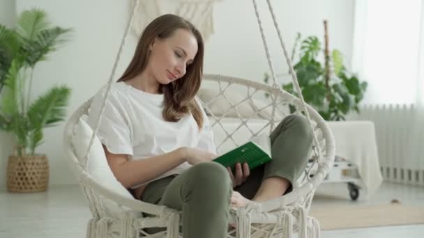 Una mujer lee un libro sentado en un columpio en casa — Vídeo de stock