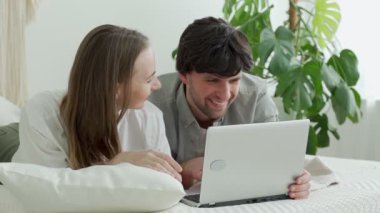 Genç evli bir çift evde yatar ve dizüstü bilgisayar kullanır ve acil konuları tartışır.