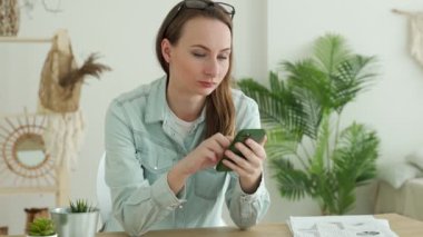 Ofiste otururken akıllı telefon kullanan esmer kadın.