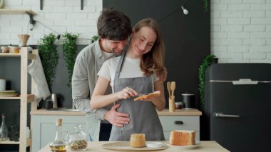 Genç bir çift sabah ekmeğe fıstık ezmesi sürüyor. Mutlu ev, aile, gıda ve sağlık kavramı.