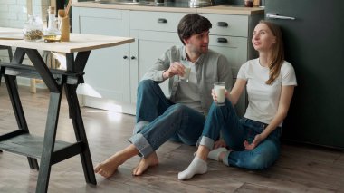 Genç çift mutfaklarının zemininde oturur ve lezzetli süt içerler.
