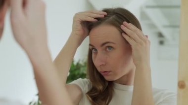 Üzgün kadın aynanın karşısında duruyor. Elindeki kırılgan ipliğe bakıyor. Doğal tıbbi şampuanın saç yapısını iyileştirdiğini düşünüyor.