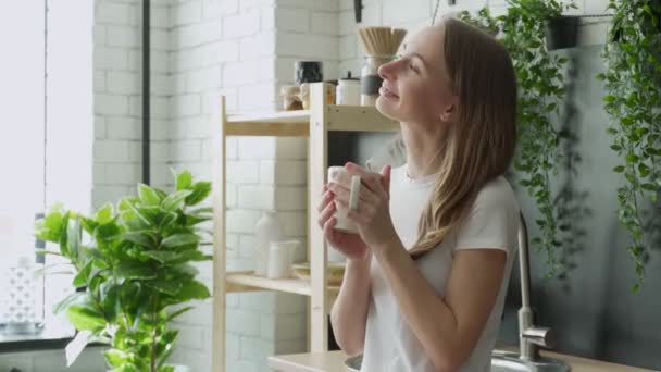 Joven mujer feliz bebe café en la cocina por la mañana en casa — Vídeos de Stock