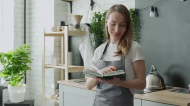 Mutfakta yemek kitabı okuyan genç bir kadın yemek tarifi arıyor.