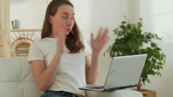 Mujer joven trabajando en la computadora en casa y celebrando la victoria, lee buenas noticias por correo electrónico con las manos levantadas y gritando — Vídeo de stock