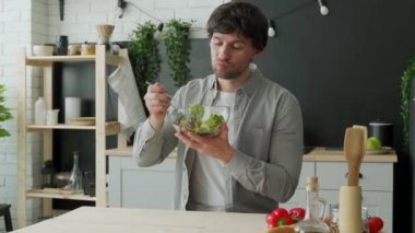 Gömlekli bir adam mutfakta salata yiyor. Sağlıklı ve vejetaryen gıda konsepti