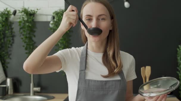 Mulher feliz saboreia sopa de uma concha e sorri na cozinha — Vídeo de Stock
