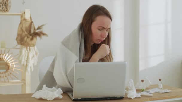 Vrouw blaast haar neus in een servet, zit aan een bureau thuis, studeert op een laptop, niest in een servet — Stockvideo