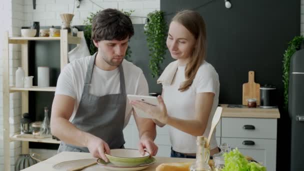 Giovani sposi usano un tablet digitale e sorridono mentre cucinano in cucina a casa — Video Stock