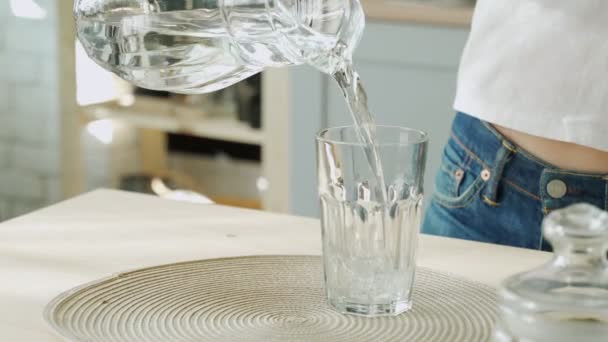Молода жінка поливає воду з глечика в склянку на кухні. Приваблива дівчина п'є воду на домашній кухні . — стокове відео