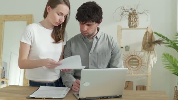 Gestresstes Paar, das frustriert wirkt, kein Geld hat, um seine Schulden zu begleichen, mit Papieren, Taschenrechner und Laptop am Tisch sitzt und Dokumente von der Bank liest — Stockvideo