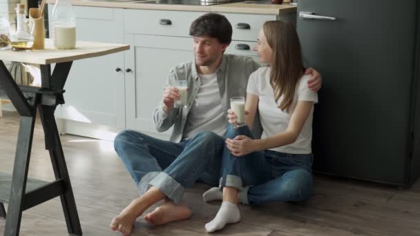 年轻夫妇坐在厨房的地板上，喝着美味的牛奶 — 图库视频影像