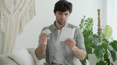 İlaçlı bir adam, yatak odasında yatağında otururken ilacın tıbbi kullanımının talimatlarını okur.