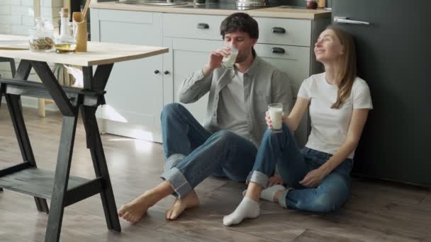 Young couple sits on the floor of their kitchen and drinks delicious milk — Stock Video