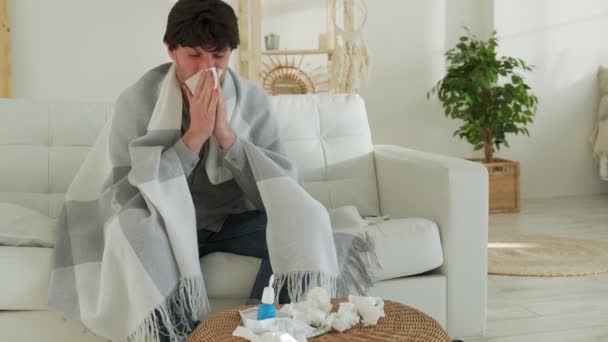 Homem embrulhado em um cobertor se sente doente com um resfriado e febre em casa, doente com gripe, sentado no sofá — Vídeo de Stock