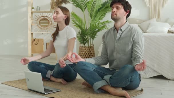 Здоровые пары тренируются дома, сидят на спортивном коврике и смотрят видео на ноутбуке — стоковое видео