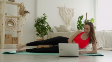 Genç bir kadının yattığı yerden bacak yükseltme egzersizlerini evde dizüstü bilgisayarla yapıyor. 