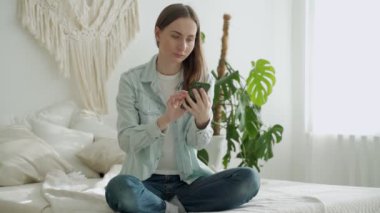 Mutlu kadın akıllı telefonu tutuyor ve evde çalışırken başarılı bir anlaşma yapıyor. Büyük para kazanan ve sevinen bir kadın. Yukarıdan para yağıyor.