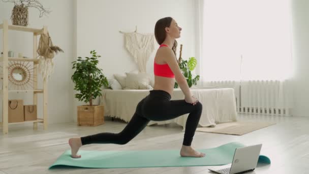 Jonge atletische vrouw in legging en top doet stretching oefeningen. Vrouw gaat in voor sport thuis. — Stockvideo