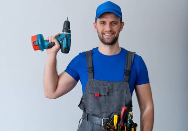 Üniformalı bakım işçisi bir tornavida tutuyor ve kameraya bakıyor. Alet kemeri takan tamirci.