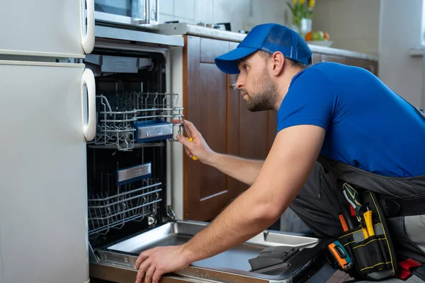 Repair of dishwashers. Repairman repairing dishwasher in kitchen