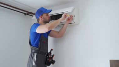Tulumlu erkek teknisyen ve mavi başlıklı adam duvardaki klimayı tamir ediyor.