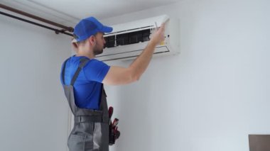Tulumlu erkek teknisyen ve mavi başlıklı adam duvardaki klimayı tamir ediyor.