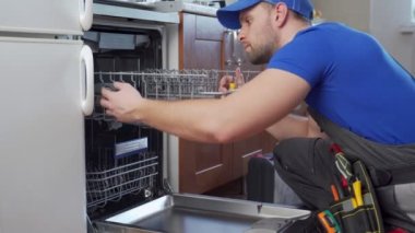 Bulaşık makinelerinin tamiri. Tamirci mutfakta bulaşık makinesini tamir ediyor.