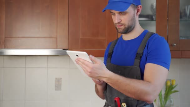 Encanador usando um cinto de ferramentas com várias ferramentas usando tablet durante o trabalho na cozinha — Vídeo de Stock