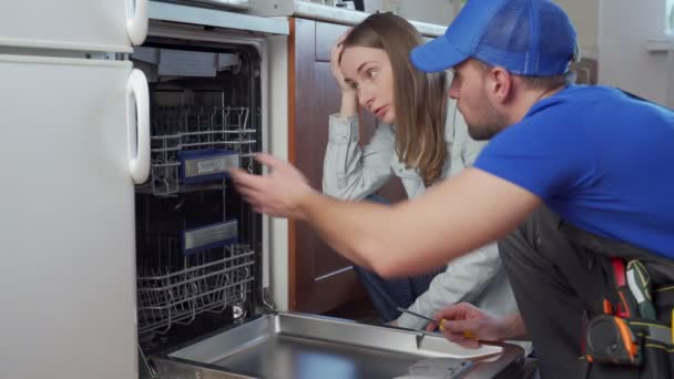 Hydraulik naprawia zmywarkę i rozmawia z gospodynią domową — Wideo stockowe