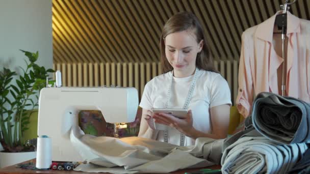 若い女性の縫い目は、縫製ワークショップでノートブック上の服の測定についてのノートを作る. — ストック動画