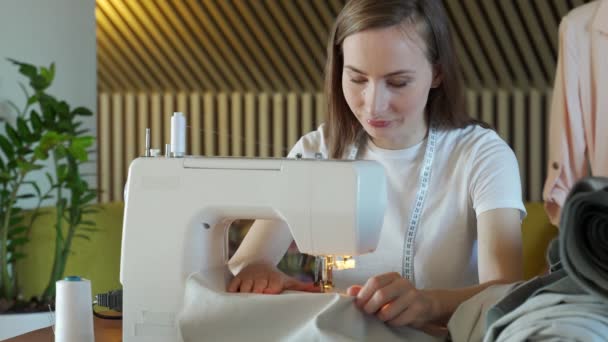 Joven costurera mujer cose en una máquina de coser sentado en una mesa — Vídeo de stock