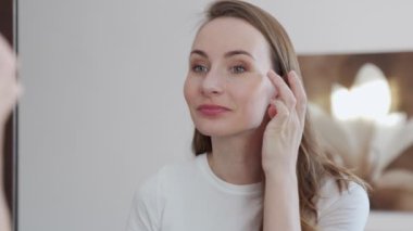 Genç bir kadın güzel sağlıklı cildine yüz kremi sürüyor. Kadın yüzüne krem sürüyor.